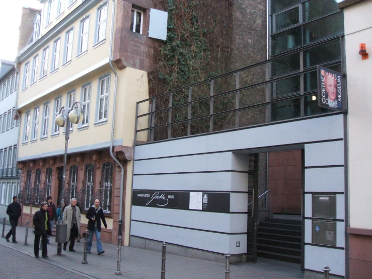 a group of people walking on the sidewalk by a tall building