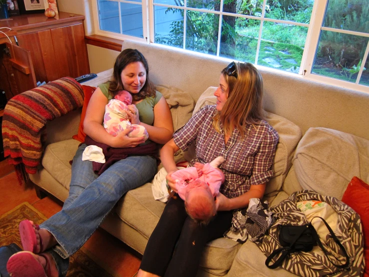 two women sitting on a couch holding their babies