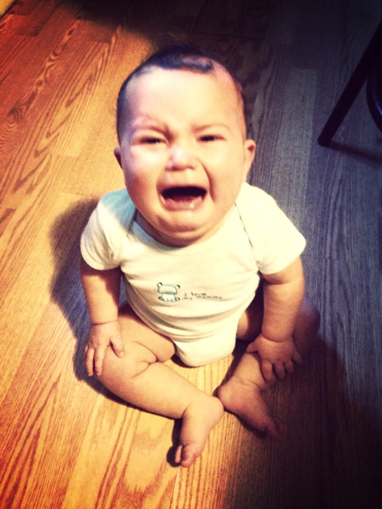 a crying baby sitting on a wood floor