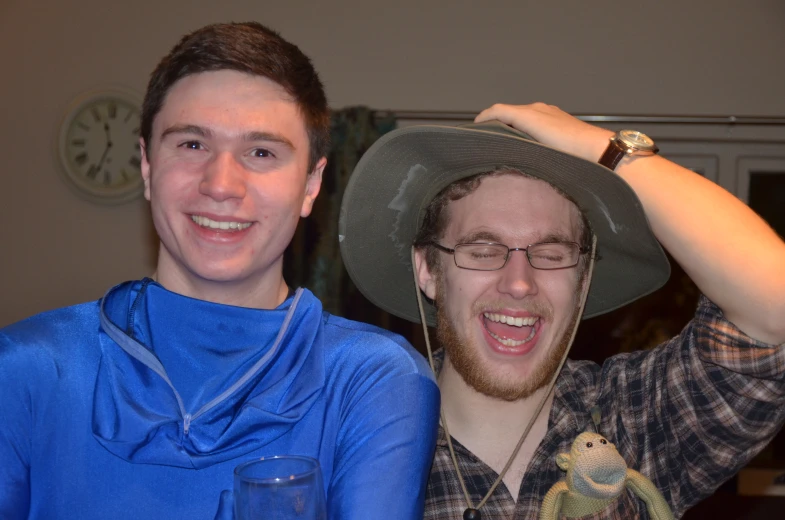 a man with a funny look and another man wearing a hat are smiling together