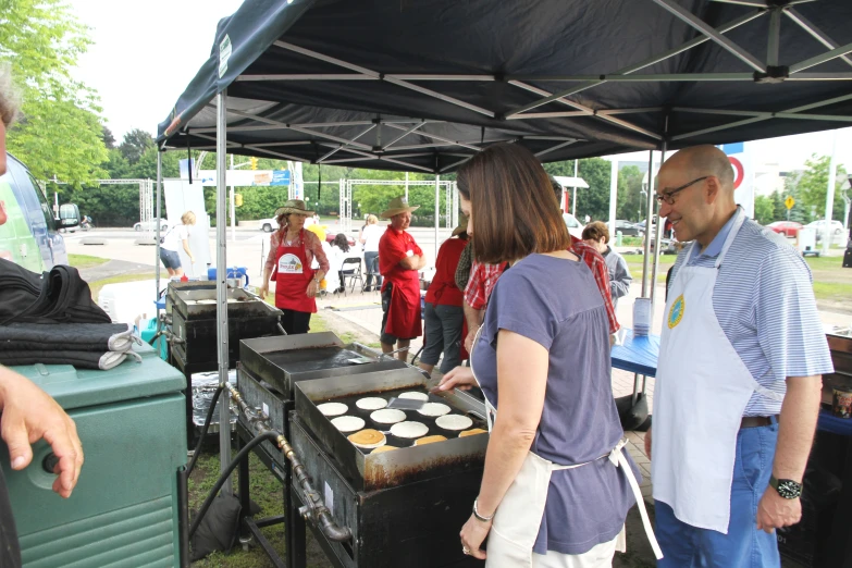 people standing under a tent preparing pies on top of a grill