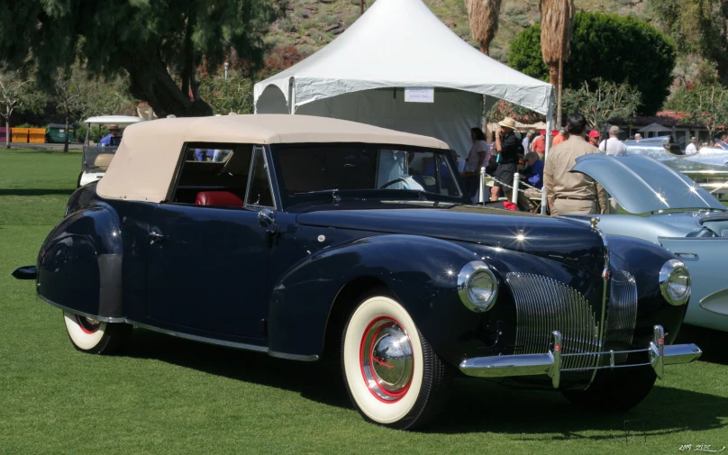 a vintage car parked in the grass near other antique cars