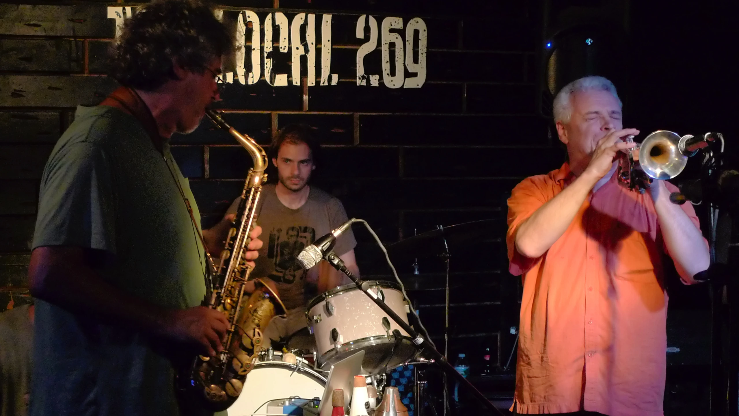 three men playing instruments and singing with an official sign in the background