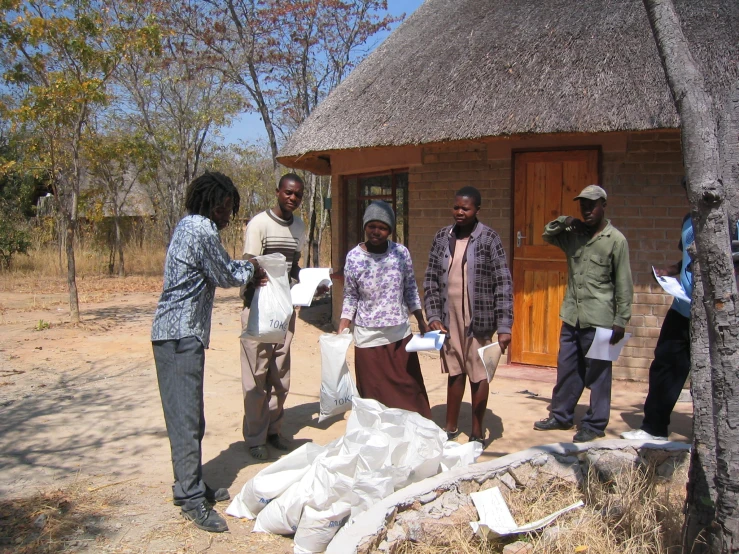 several people are standing in front of a hut that is constructed out of brick