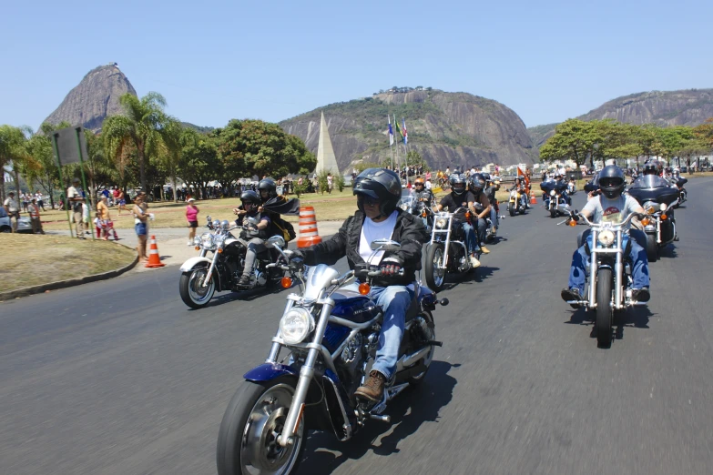 motorcycles riding down the road with people standing near