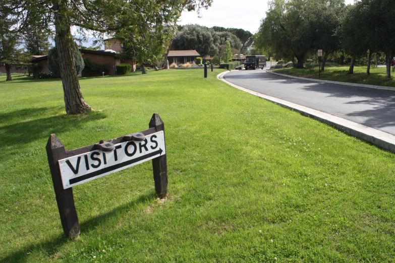 a small park with a lawn that has a street sign that says visitors