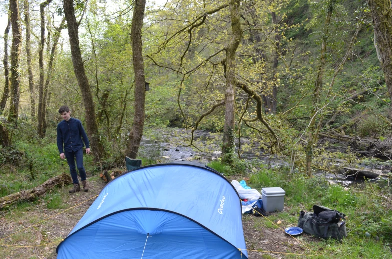 a person is standing next to a blue tent in the woods