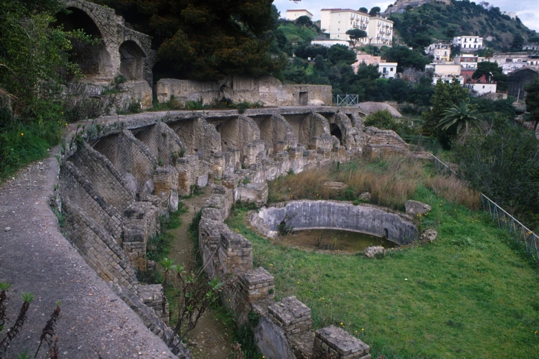 a roman colliseum overlooking a city with green trees and grass