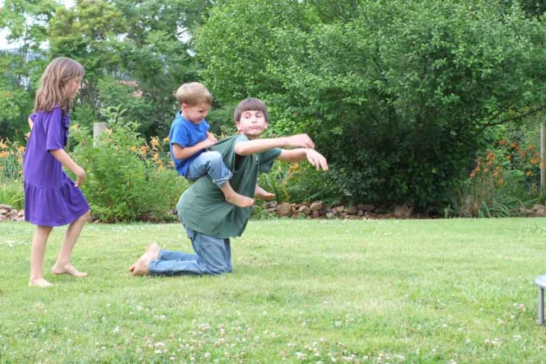 three children on the grass, one holding his legs high and the other sitting in the air