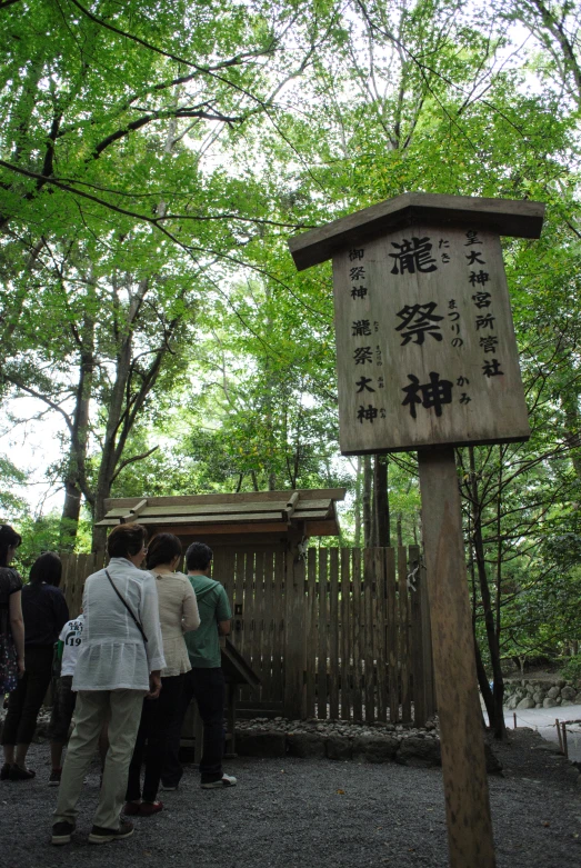 many people are gathered outside by a wooden sign