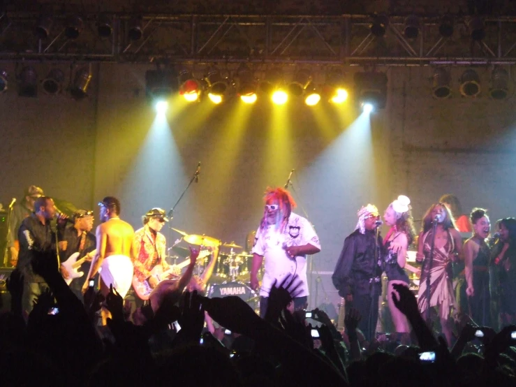 the man in white suit is singing to his band on stage