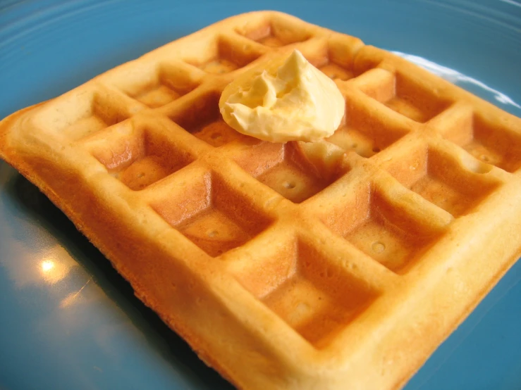 a waffle on a blue plate has cream on it