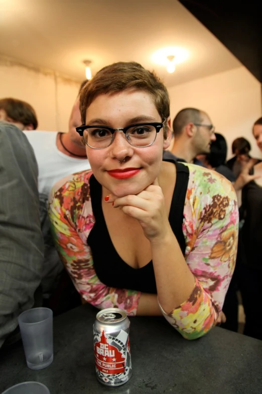 woman in glasses leaning her chin on top of a table with a can of drink