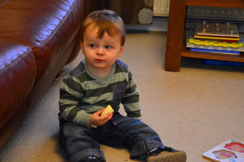 a boy is sitting on the floor eating a banana