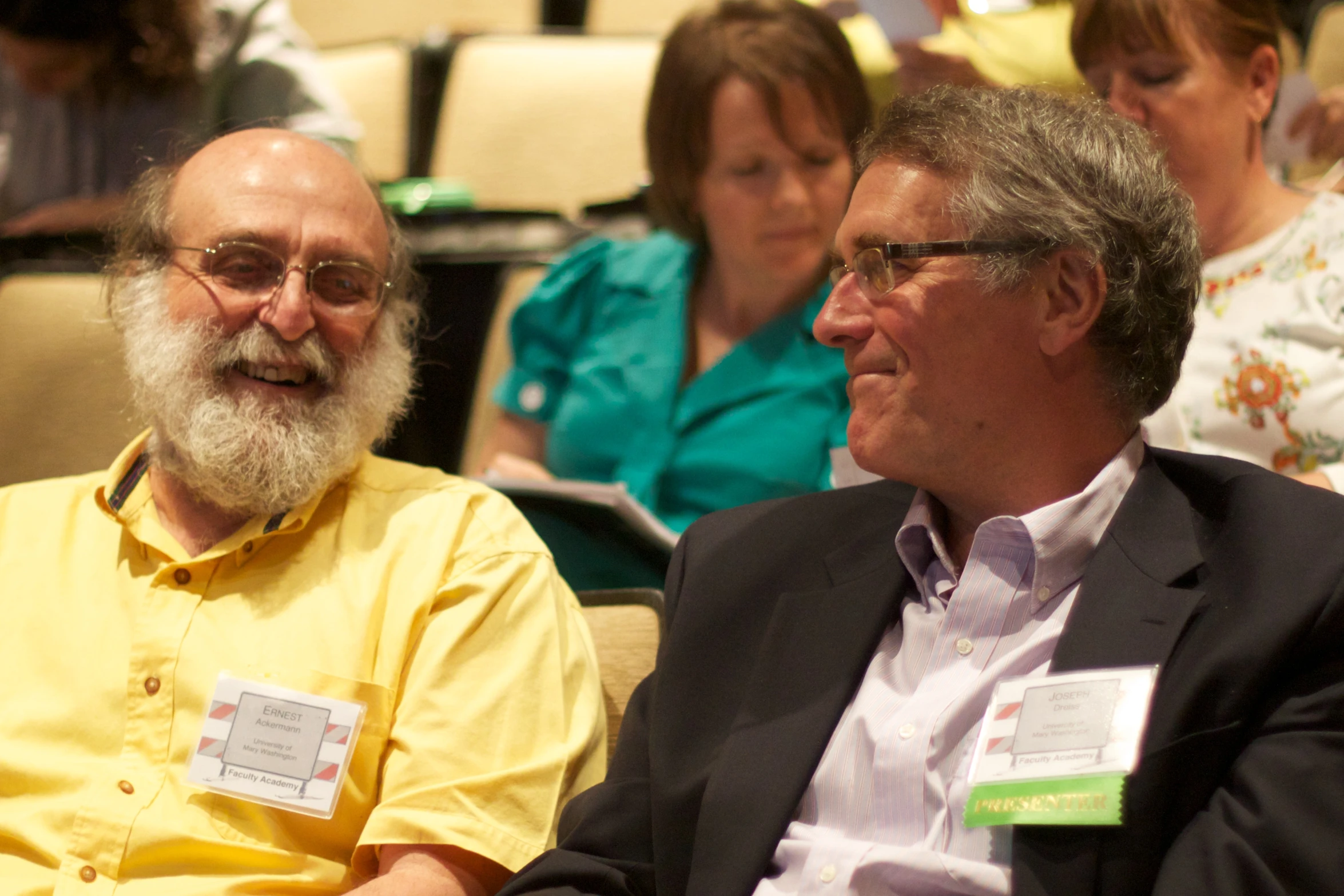 the man with a white beard sits next to another man wearing glasses