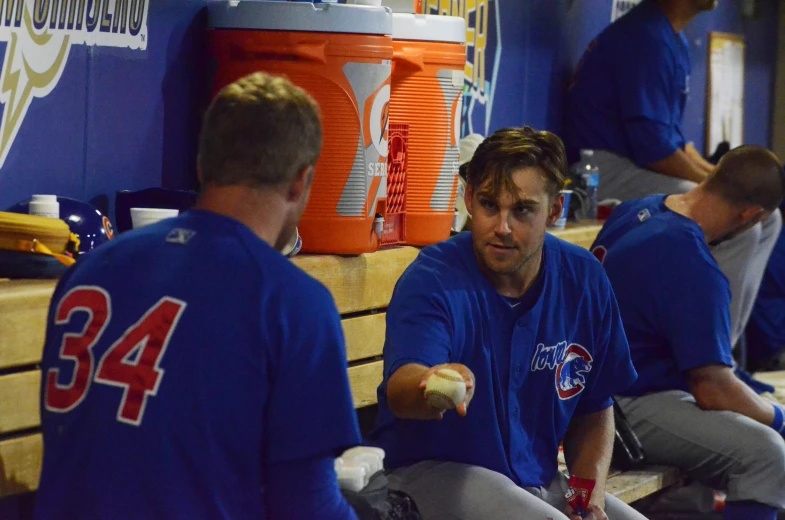 two guys in the dugout one holds food in his hand and another is eating soing out of his other hand