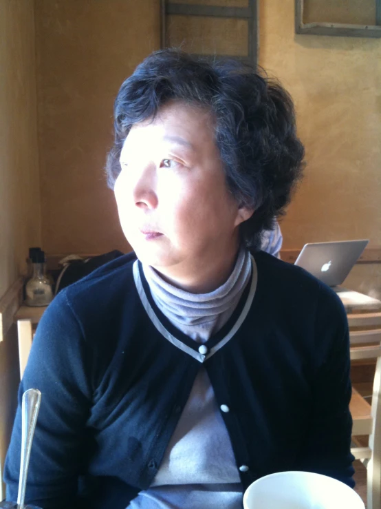 woman with black hair and white sweater sitting at a table with cup in front of her