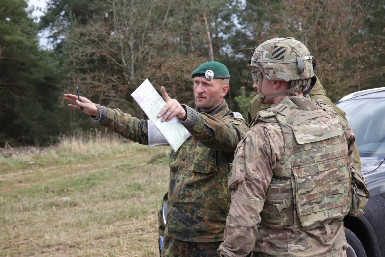 two military men are talking in front of the vehicle