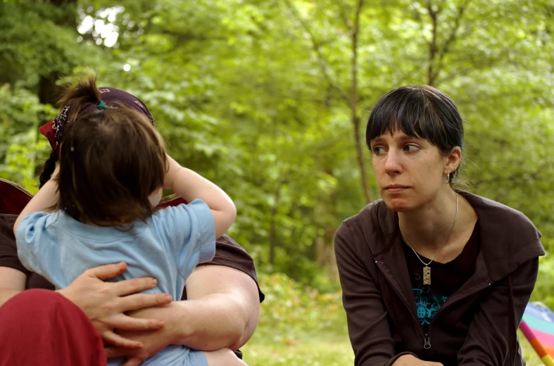 a woman sits with two children in a park