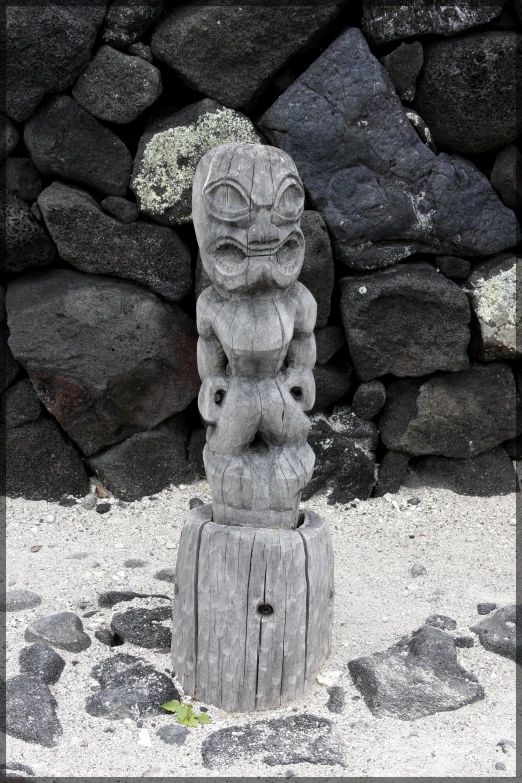 a wooden statue sits between two stacked rocks