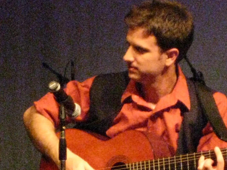 the man is playing his guitar and singing into the microphone
