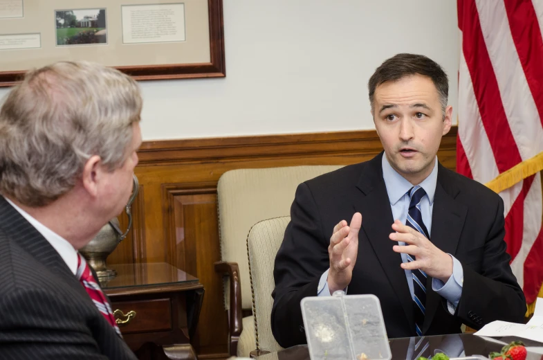 the man is sitting at the table in a suit talking to someone