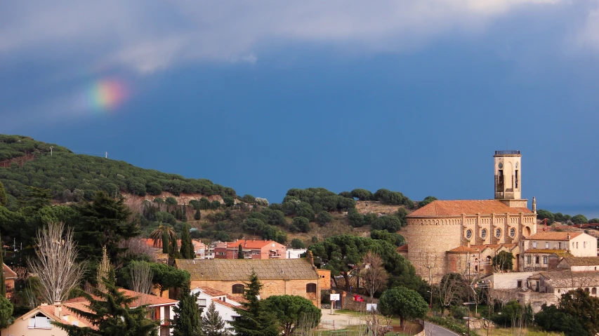 a scenic city is perched on a hillside with a tree - lined hill in the background