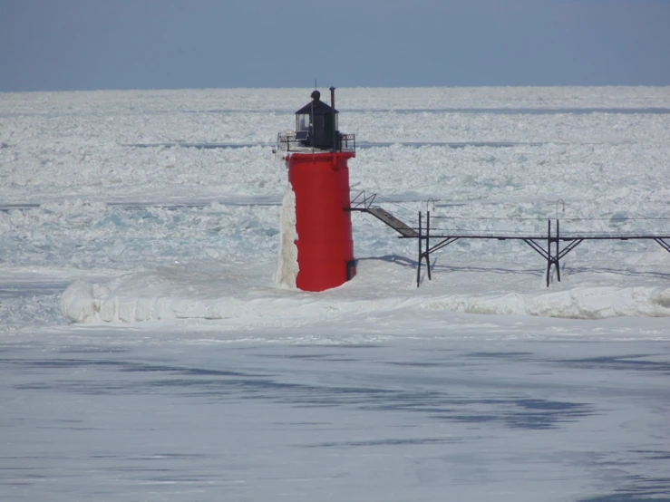 a red light house on the shore with snow