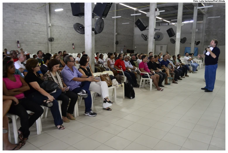 a crowd of people sitting in chairs watching someone giving a presentation