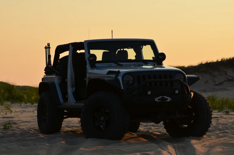 a jeep is on the beach as the sun goes down