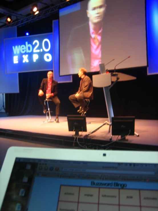 two men sitting on a chair while using laptops