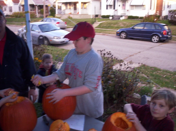 some children are carve pumpkins outside by some cars