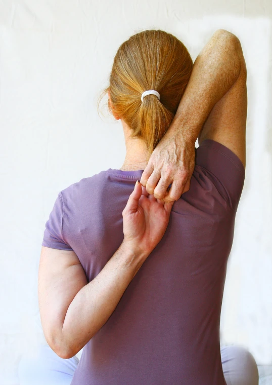 a woman sits on the ground holding her hands over her shoulders