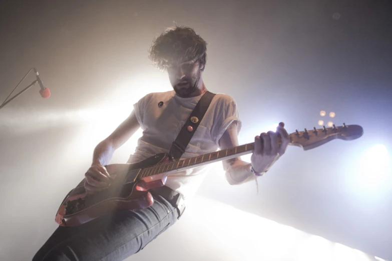 a young man plays an electric guitar in front of a spotlight