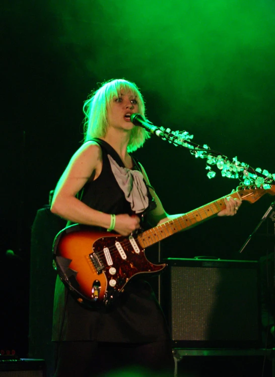 a woman with long blonde hair playing an electric guitar on stage