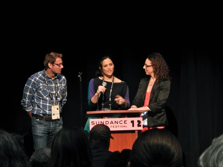 two woman and a man standing at a podium with microphones