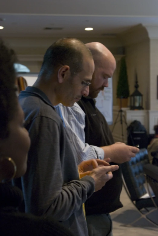 three men standing near each other looking at their cell phones