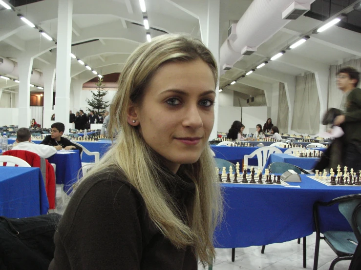 a beautiful young lady standing in front of a table full of chess