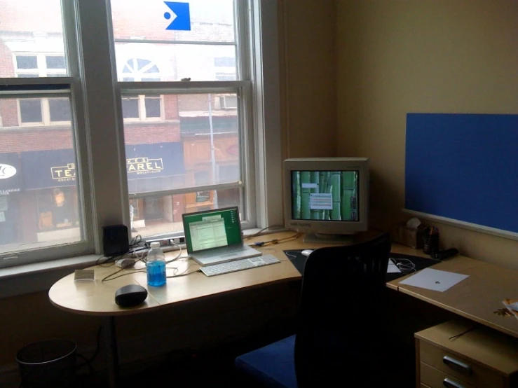 a computer sits on a desk near two windows