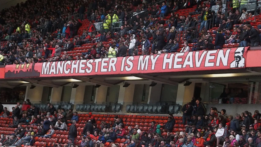 a man is standing at a football stadium with a sign in his hand reading manchester is my heaven?
