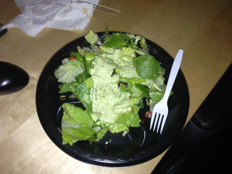 a black plate topped with a salad covered in lettuce and dressing