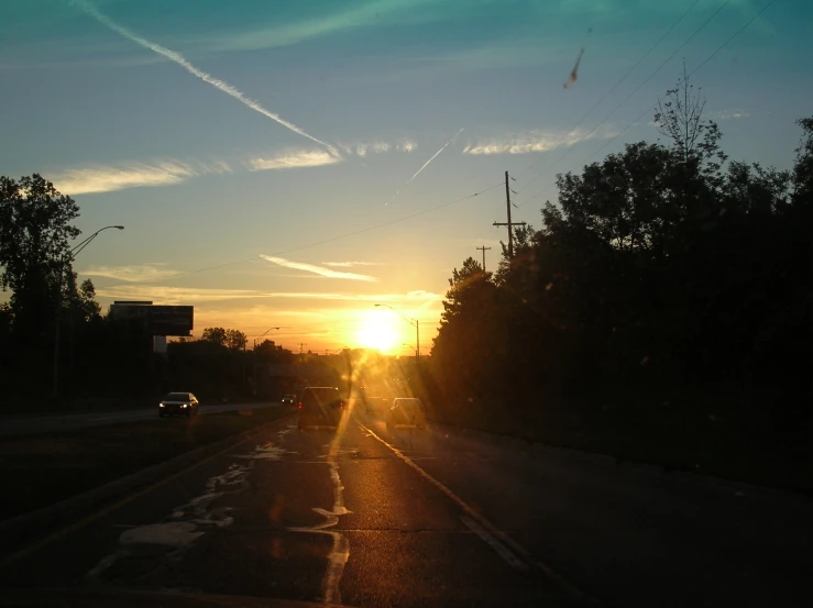 the sun sets in an orange light along a street