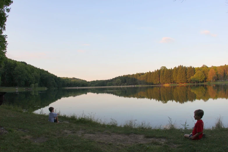 two s are sitting on the shore near a body of water