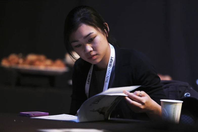 a woman holding a white cup looking at a book