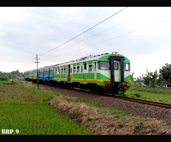 a green and blue train traveling past lush green fields