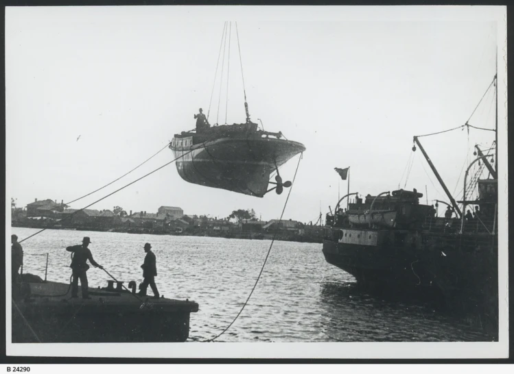 three people watch as a large boat is suspended by ropes