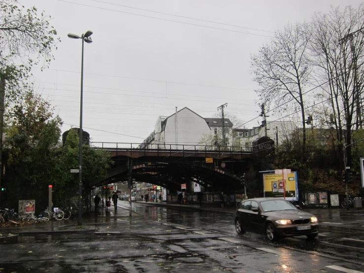 a city street with cars, a pedestrian bridge and people crossing