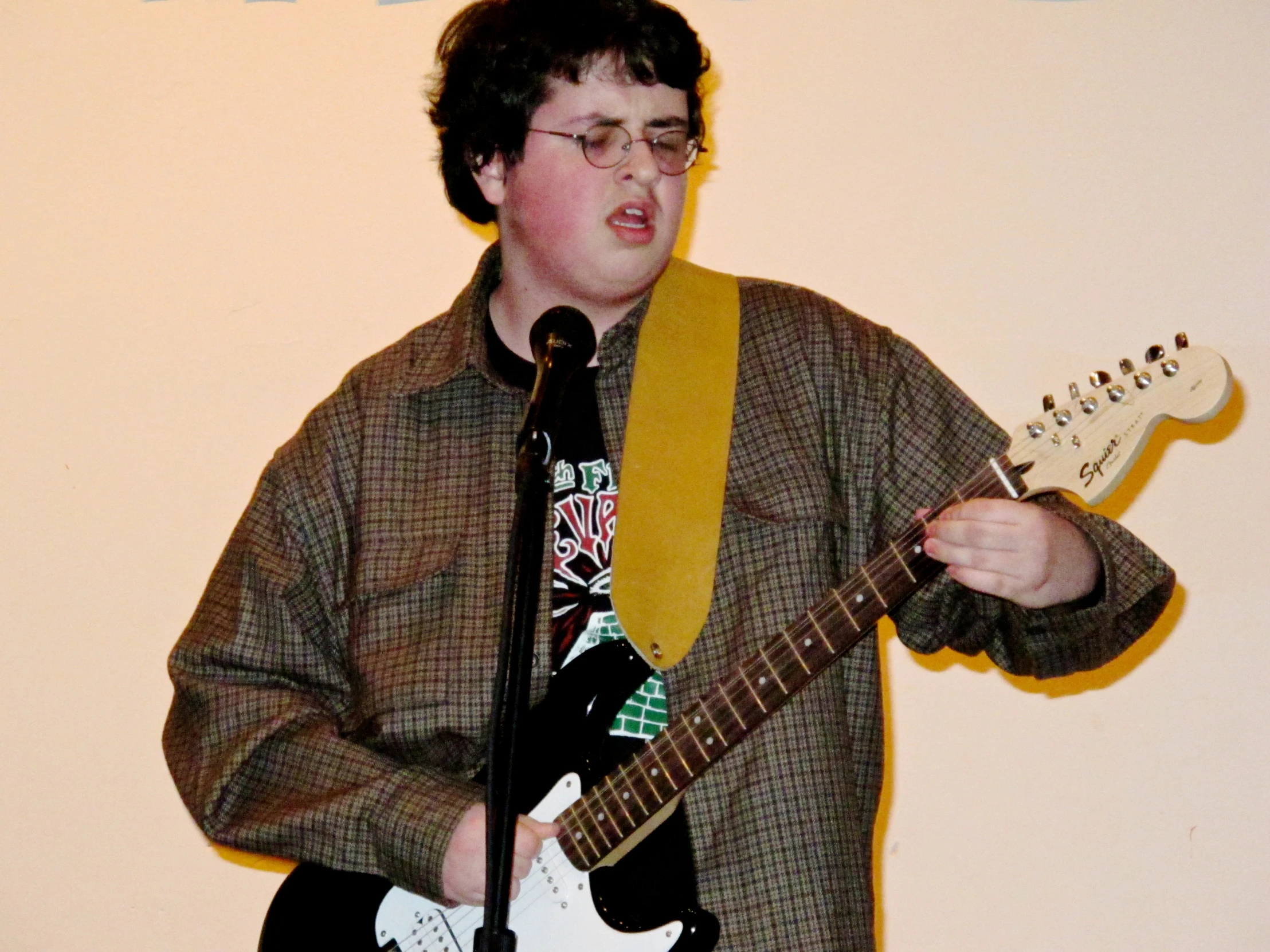 a boy with glasses playing a guitar while standing in front of a microphone