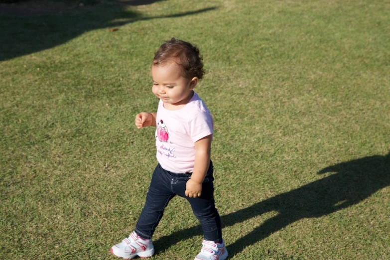 a little girl walking in the grass on top of a sunny day