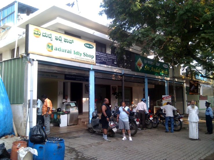 several people are outside of the shop with motorcycles